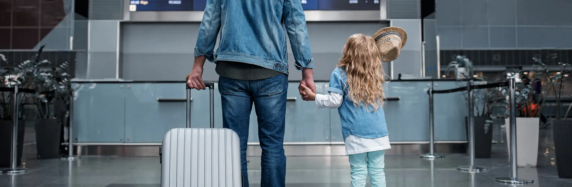 Padre e hija tomados de la mano en el aeropuerto con maleta de viaje